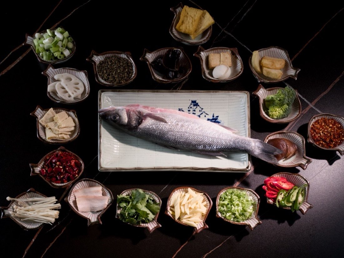 A whole sea bass among small dishes of hotpot ingredients
